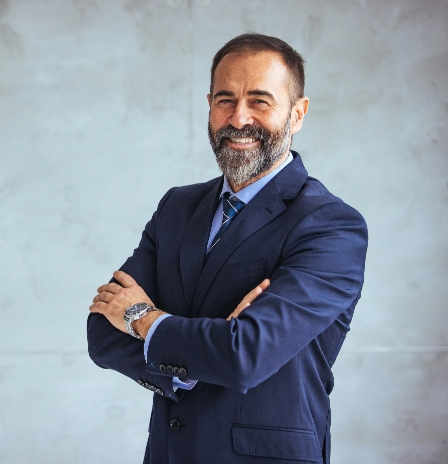 Person in a white shirt with arms crossed standing against a blue background.